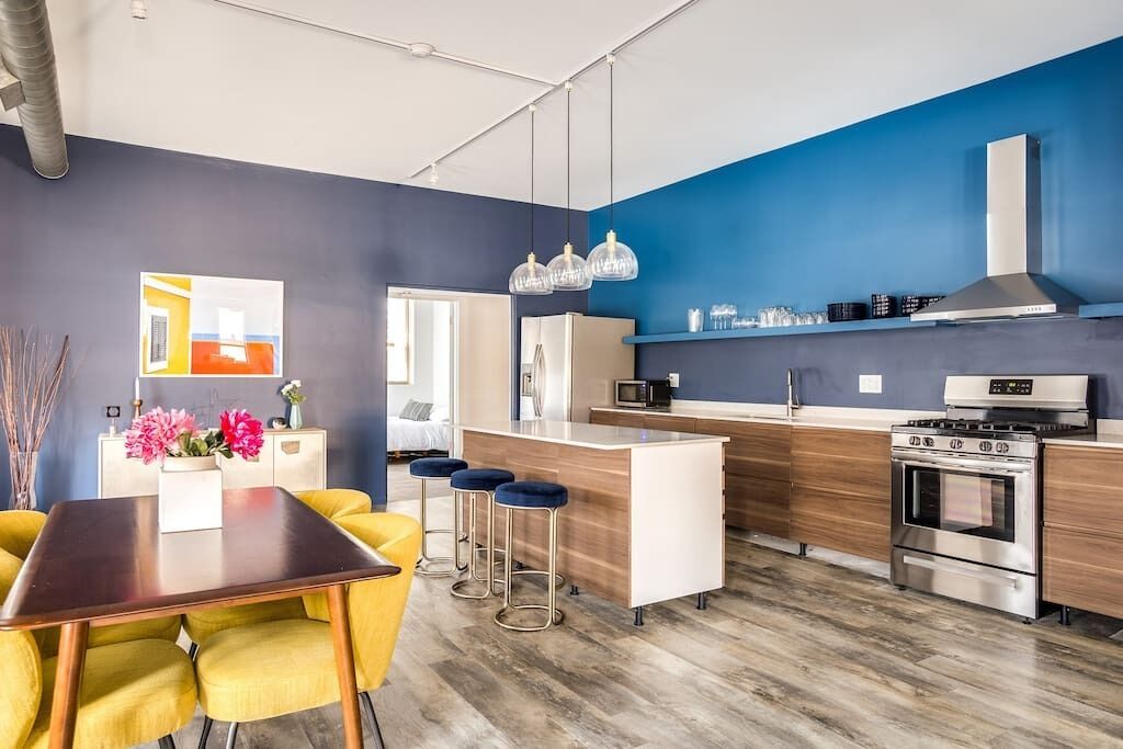 Una cocina moderna con una isla central, taburetes de bar y una mesa de comedor con sillas amarillas.