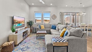 A modern living room with a large flat-screen TV, a ceiling fan, and a large window with a view of the desert. - Ocotillo Springs Resort 69: 3bd, 3.5 bath with a Private Hot Tub, Fire Pit, and Private Patio (Santa Clara)