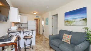 A compact living space with a kitchenette, a gray couch with a beach-themed pillow, and a painting of a beach scene. - AUGUST 8 TO 11 AVAILABLE ...  FAMILIES/COUPLES ONLY  
CUTE UNIT WITH POOL (Seaside Heights)