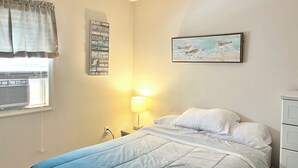 A bedroom with a bed, a bedside lamp, a wall-mounted artwork, and a window with an air conditioner. - AUGUST 8 TO 11 AVAILABLE ...  FAMILIES/COUPLES ONLY  
CUTE UNIT WITH POOL (Seaside Heights)