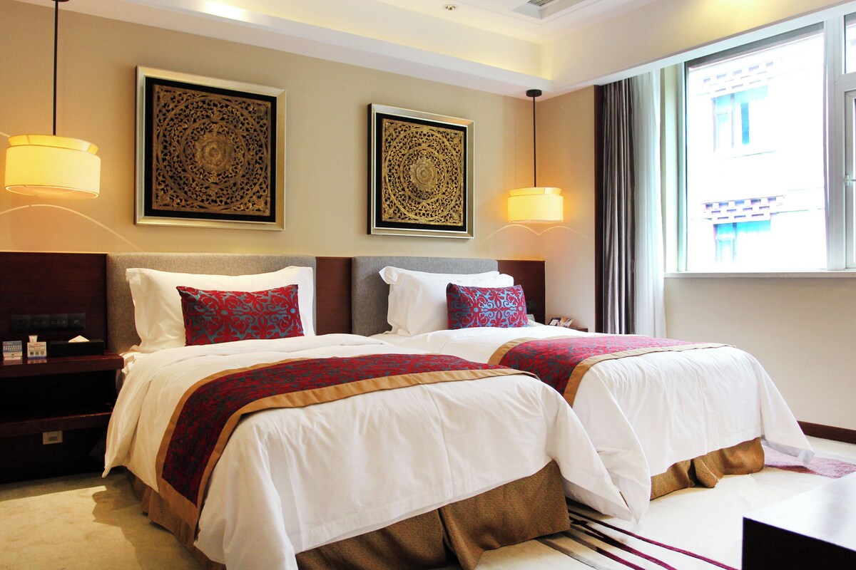 A hotel room with two beds, a nightstand, and two wall-mounted lamps.