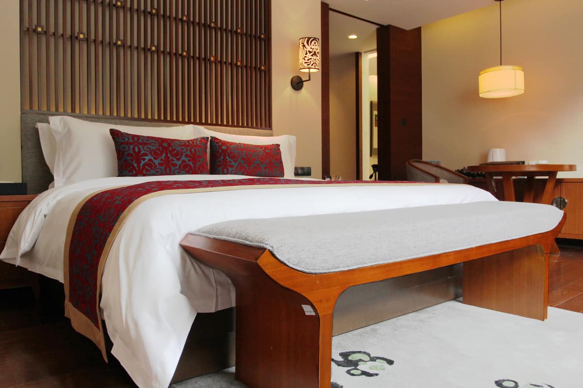 A hotel room with a large bed, a wooden bench, a desk, and a chair.