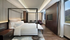 A modern hotel room with a four-poster bed, a flat-screen TV, a seating area, and a view of the outdoors. - Crowne Plaza Yading by IHG (Garze)