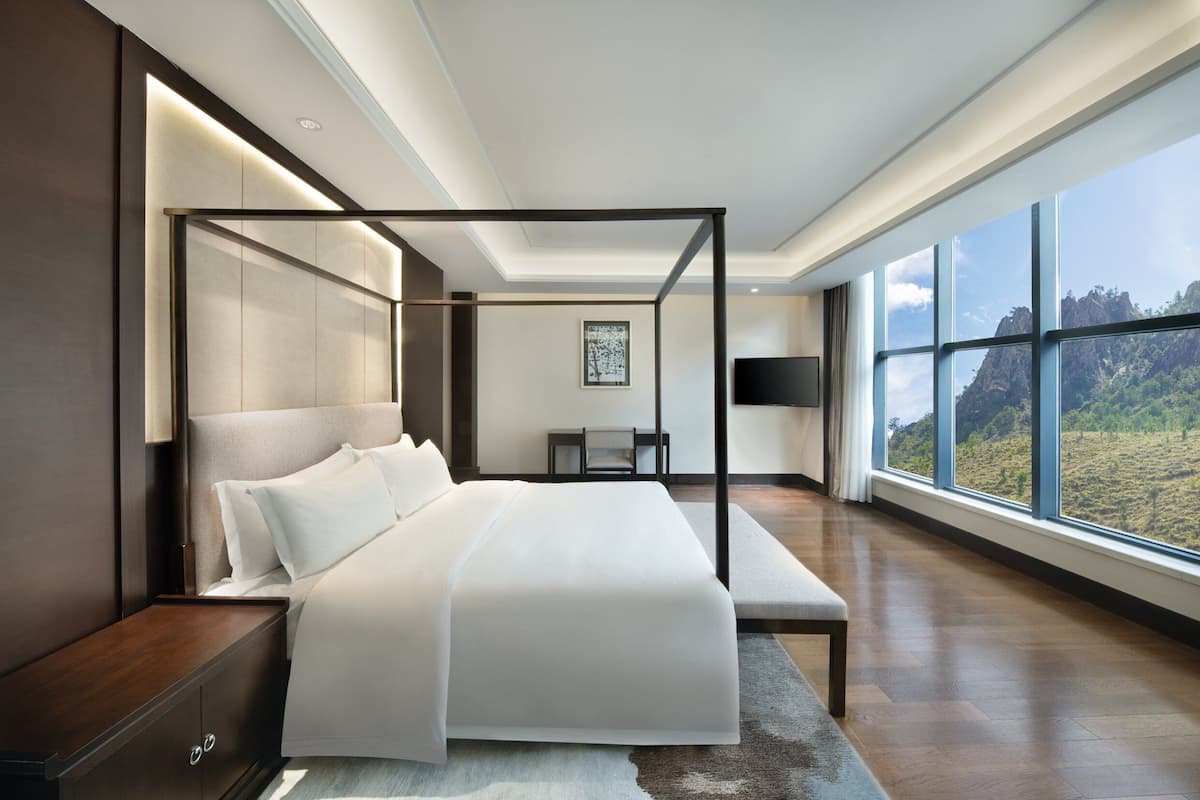 A modern bedroom with a four-poster bed, a large window offering a view of the outdoors, and a minimalist design.