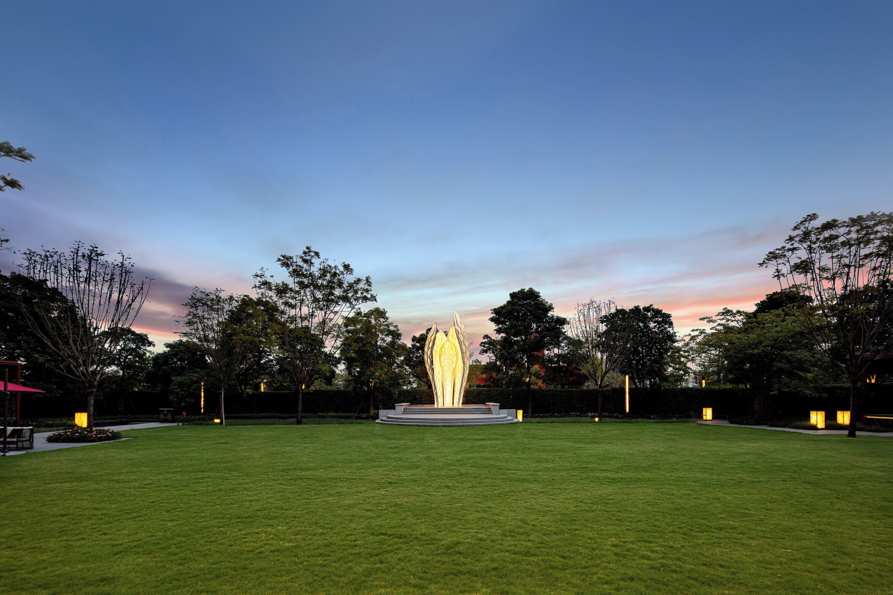 A well-maintained lawn with a central fountain, surrounded by trees and a clear sky.