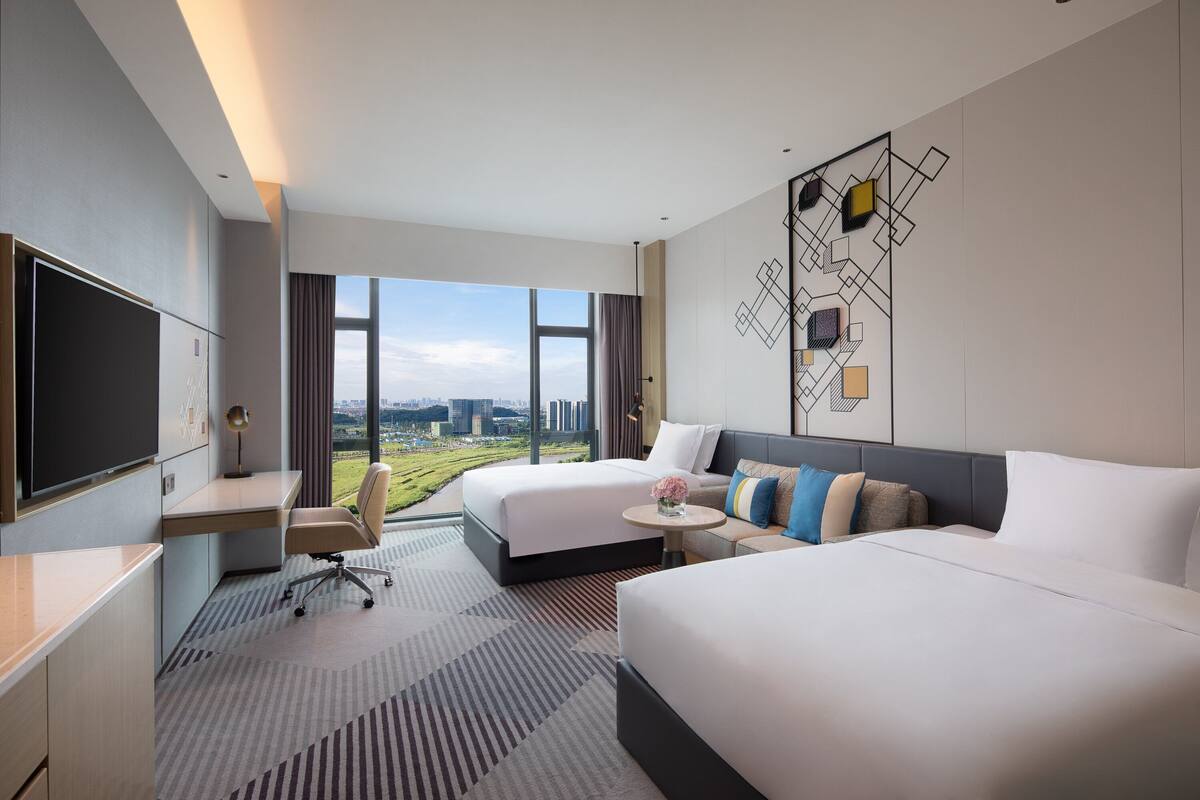 Une chambre d’hôtel avec deux lits, un bureau, une chaise et un grand téléviseur.