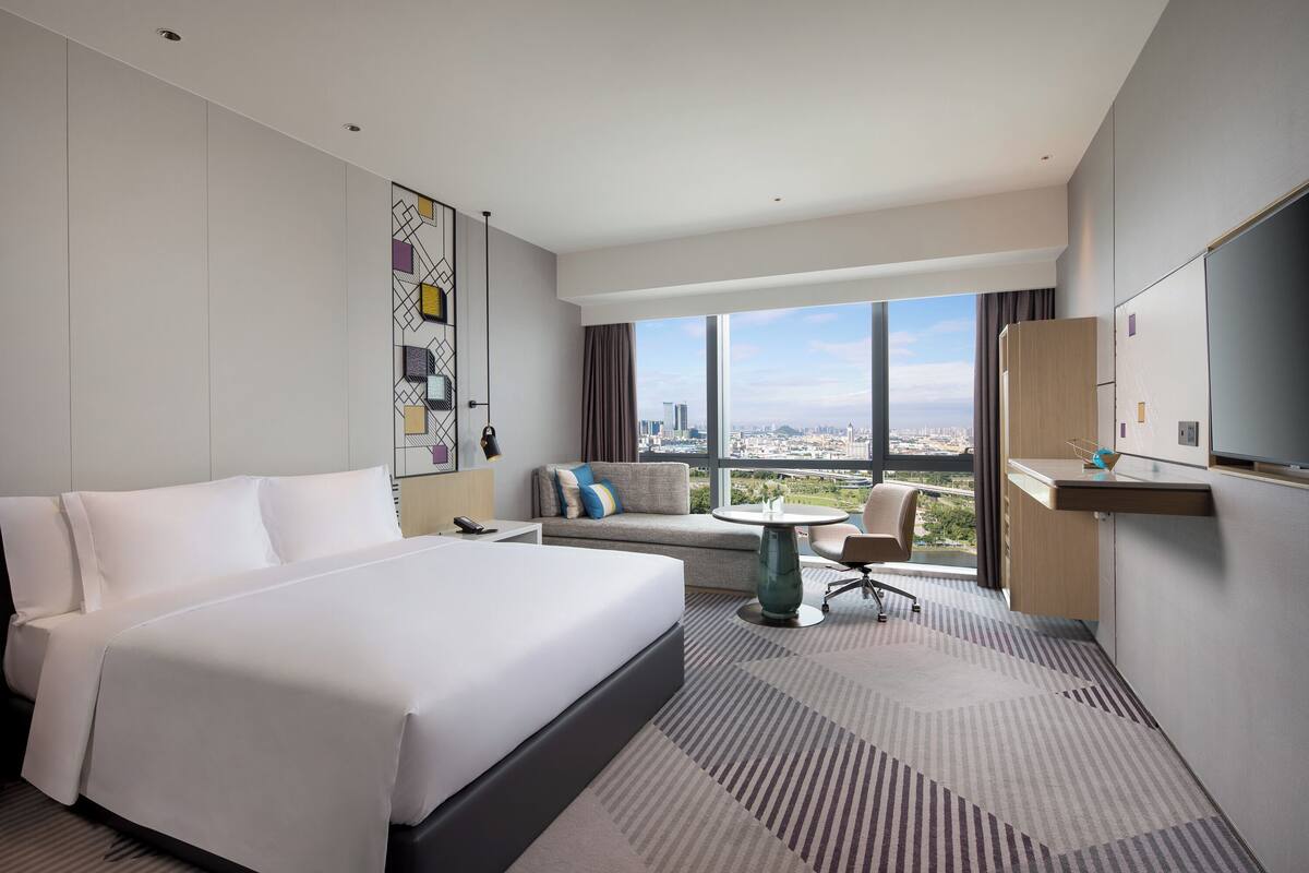 Une chambre d’hôtel moderne avec un grand lit, un canapé, une petite table et un téléviseur.