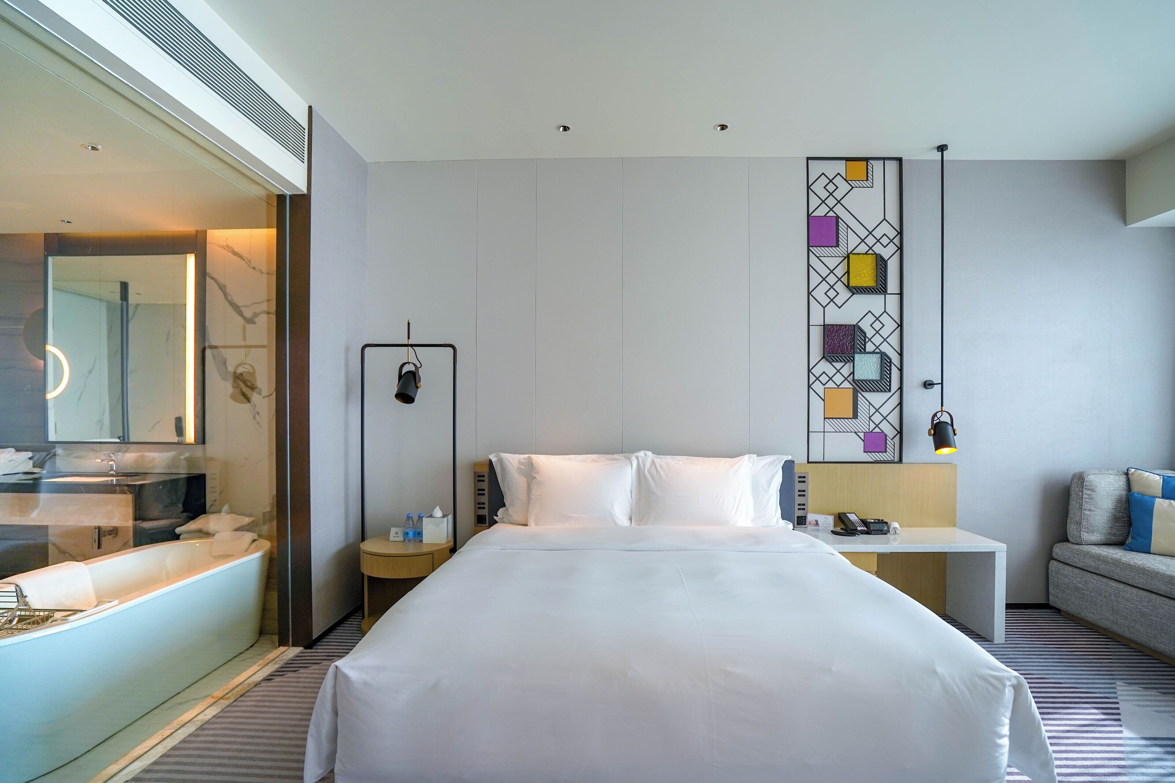 Una habitación de hotel moderna con una cama grande, una mesita de noche, un escritorio y un sofá.