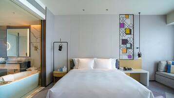 Una habitación de hotel moderna con una cama grande, una mesita de noche, un escritorio y un sofá.