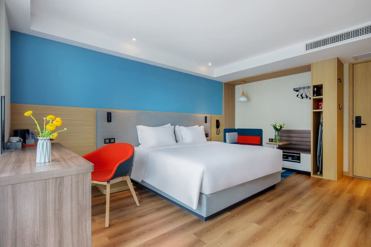 A modern hotel room with a large bed, a desk, and a chair.