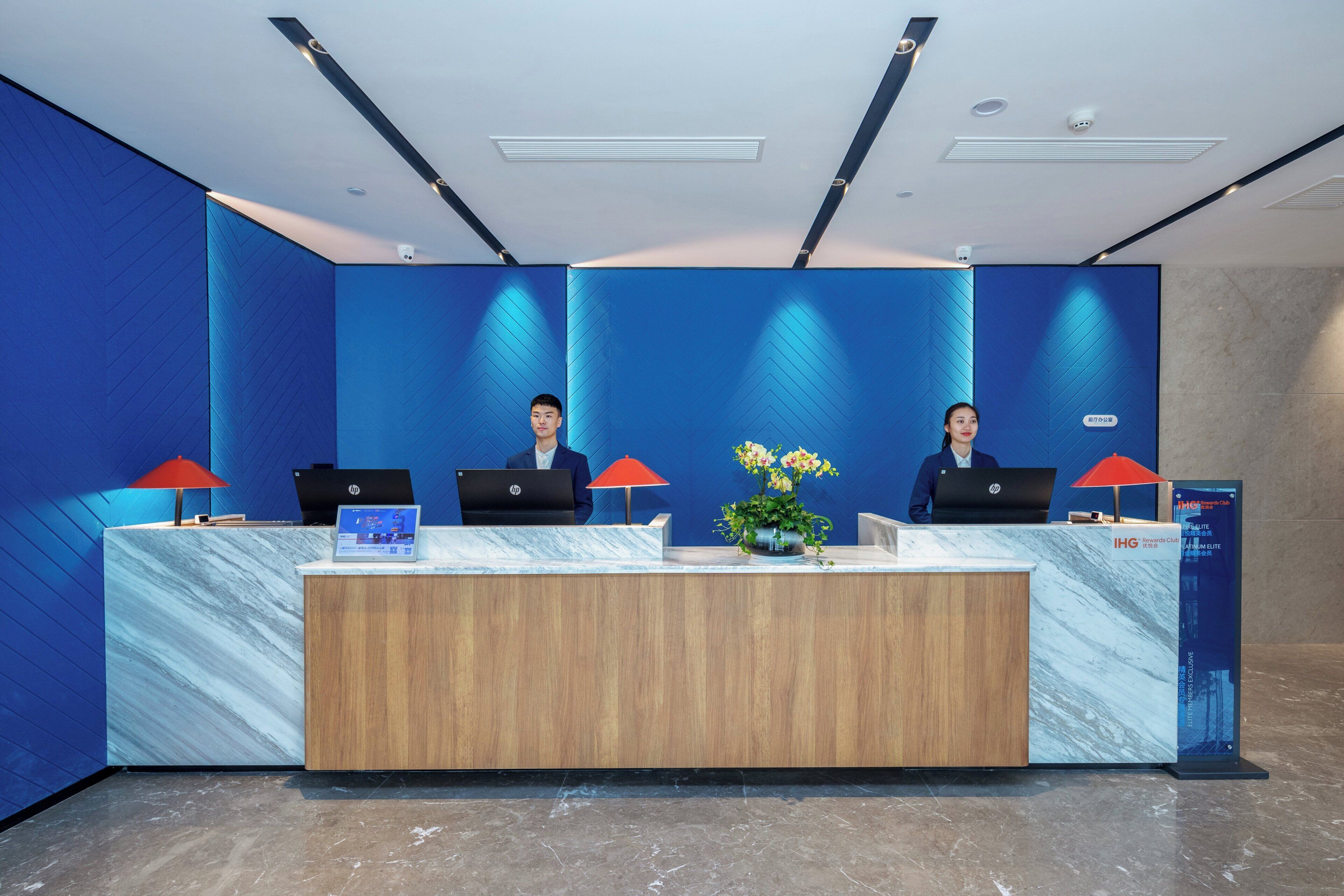 Una recepción con dos empleados, pared azul y suelo de mármol.