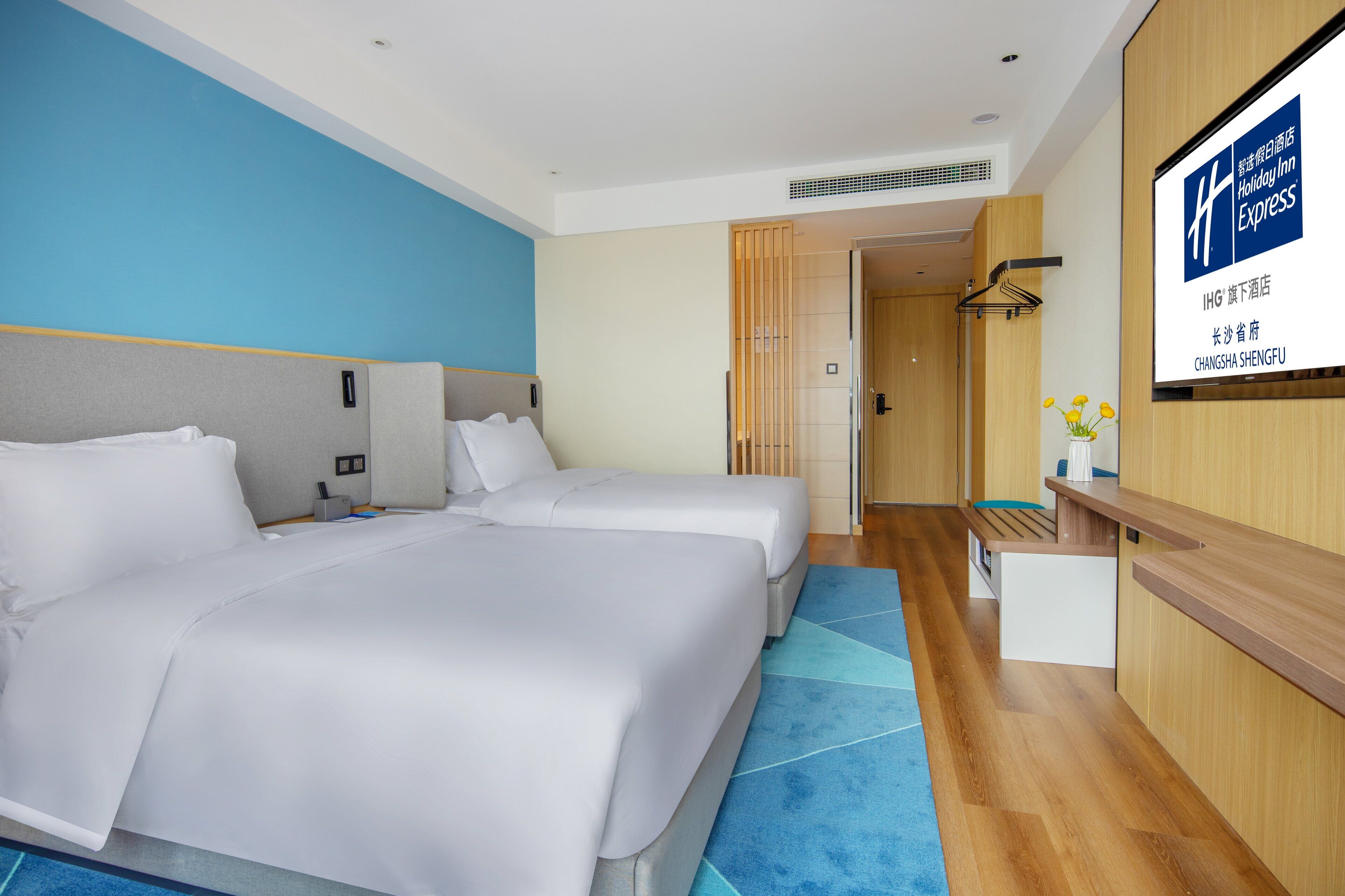 A hotel room with two beds, a desk, and a shower area.