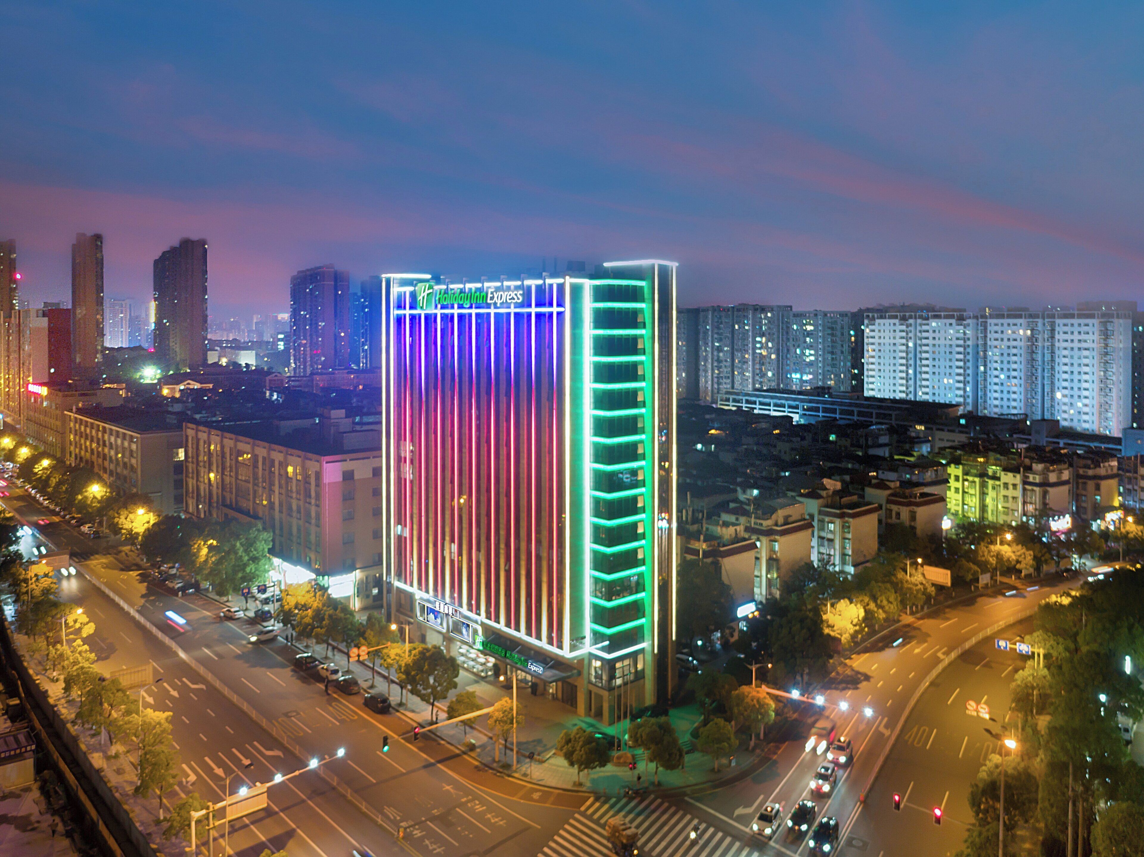 A high-rise building with a distinctive vertical light display, surrounded by a cityscape with other tall buildings and a busy street.
