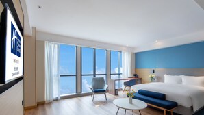 A modern hotel room with a large bed, a sofa, a small table, and a chair. There is a large window offering a view of the sky. - Holiday Inn Express Changsha Shengfu by IHG (Changsha)