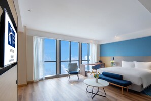A modern hotel room with a large bed, a sofa, a small table, and a chair. There is a large window offering a view of the sky. - Holiday Inn Express Changsha Shengfu by IHG (Changsha)
