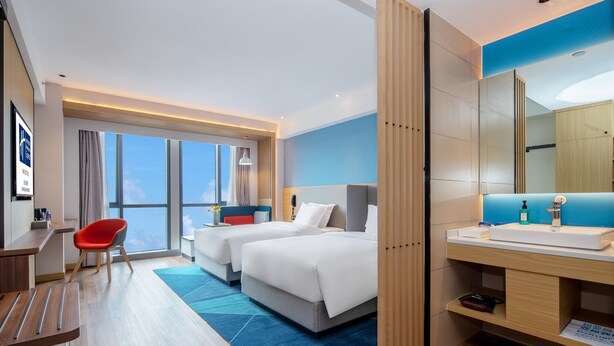 A hotel room with two beds, a desk, a chair, a large window, and a bathroom with a sink and mirror. - Holiday Inn Express Changsha Shengfu by IHG (Changsha)