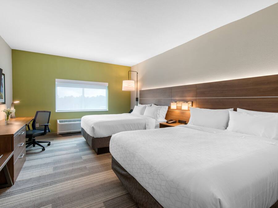 A hotel room with two beds, a desk, a chair, a TV, and a window with a view.