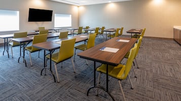 A conference room with tables and chairs, a flat-screen TV, and a projector screen.