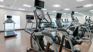 A gym with multiple treadmills and elliptical machines, equipped with digital screens and control panels.