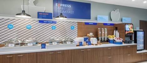 Zona de desayuno tipo buffet con secciones identificadas para comida caliente, cereales, fruta y huevos.