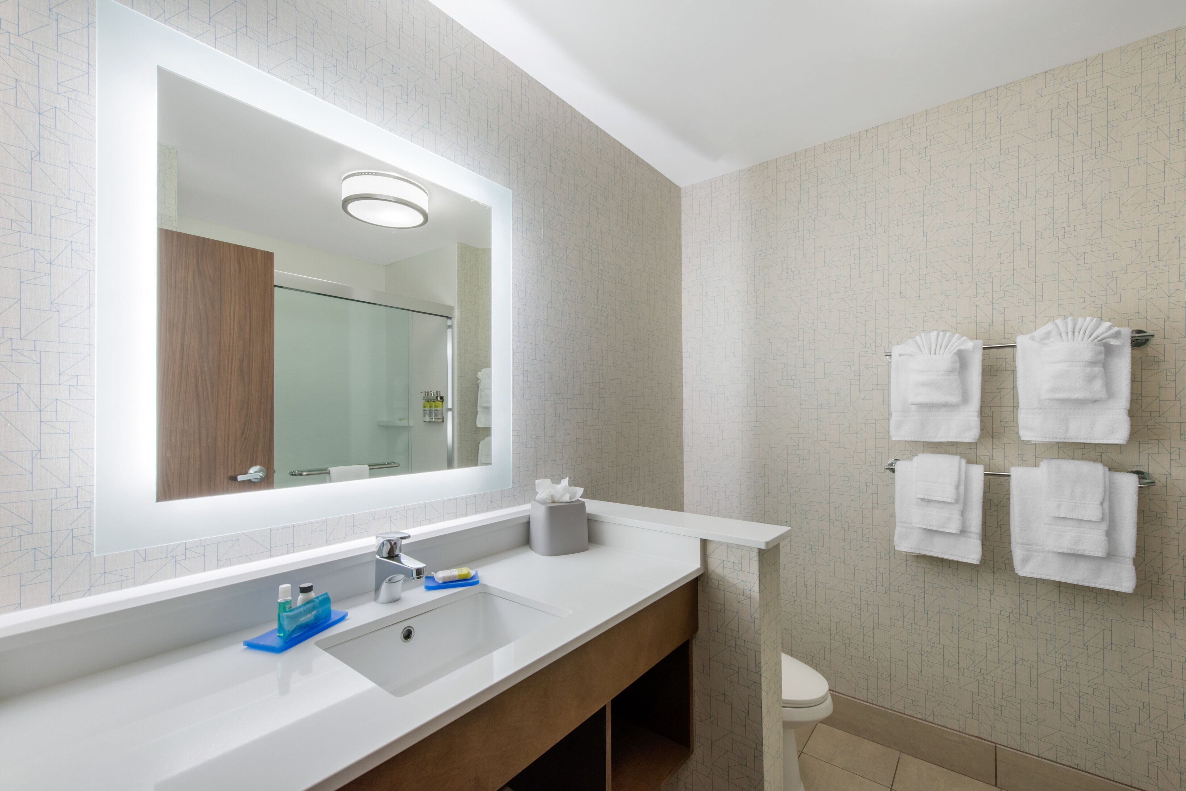 A modern bathroom with a large mirror, white sink, and towel rack.