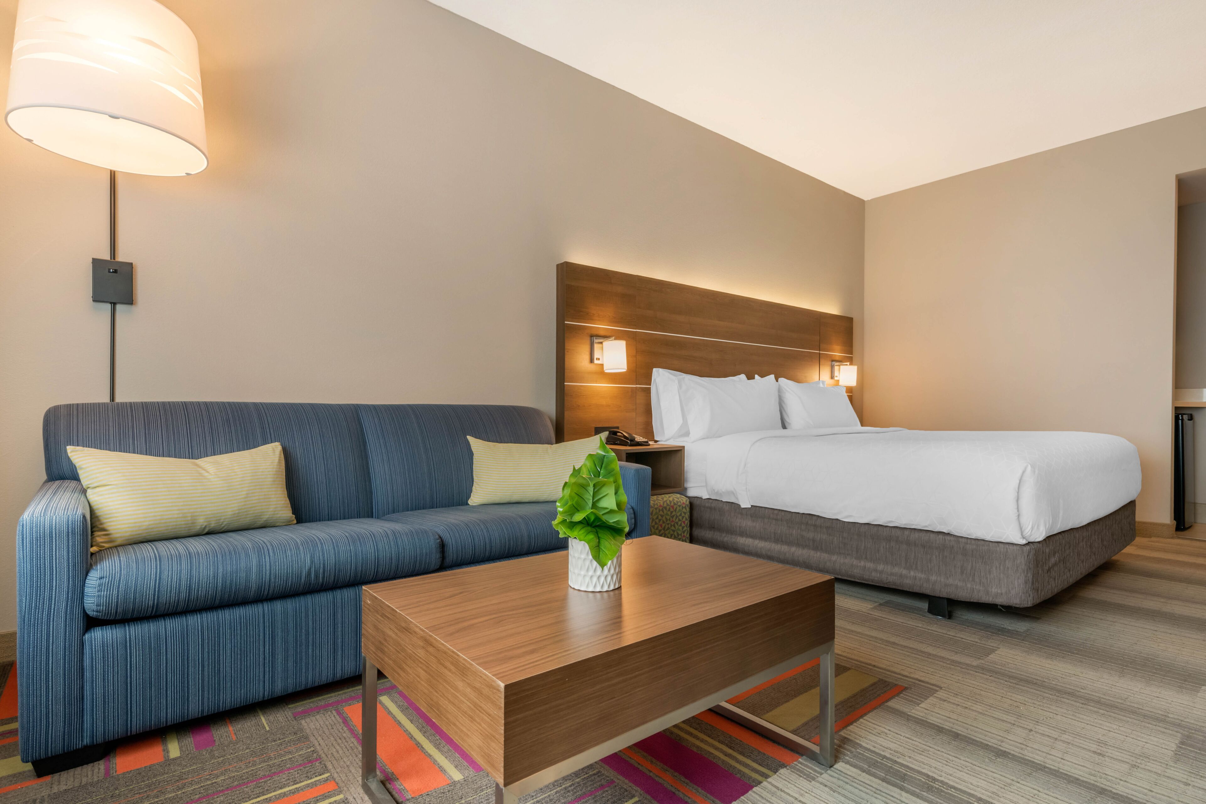 Quarto de hotel com sofá, cama, mesa de centro de madeira e luminária.