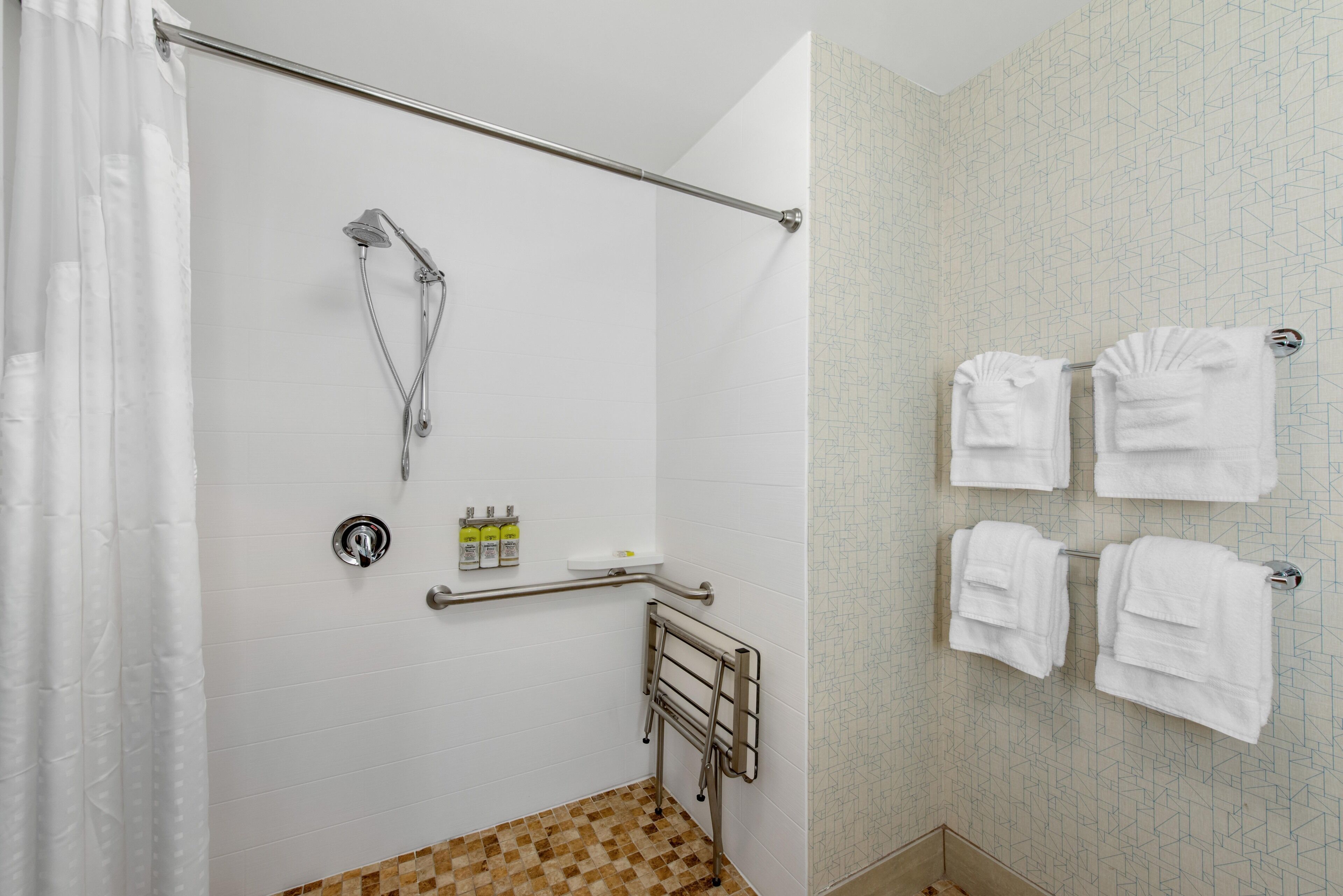 Een badkamer met een douche, handgrepen en handdoeken op een rek.