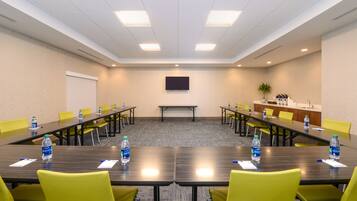 A conference room with a long table, yellow chairs, water bottles, and a flat-screen TV on the wall.