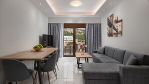 A modern living room with a grey sofa, a wooden dining table with chairs, and a view of a hillside through a glass door. - Villa Divina (Rhodes)