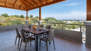 A covered outdoor patio with a wooden table and wicker chairs, overlooking a scenic landscape. - Villa Divina (Rhodes)