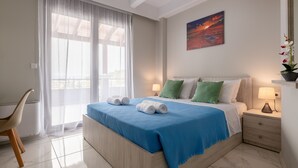A neatly made bed with a blue blanket and two rolled towels, a bedside table with a lamp, a chair, and a window with sheer curtains. - Villa Divina (Rhodes)