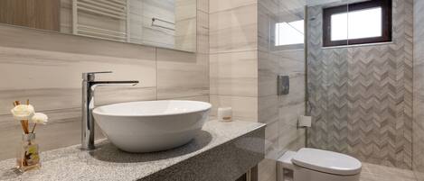 Un baño moderno con un lavamanos grande tipo recipiente, un espejo y un inodoro.