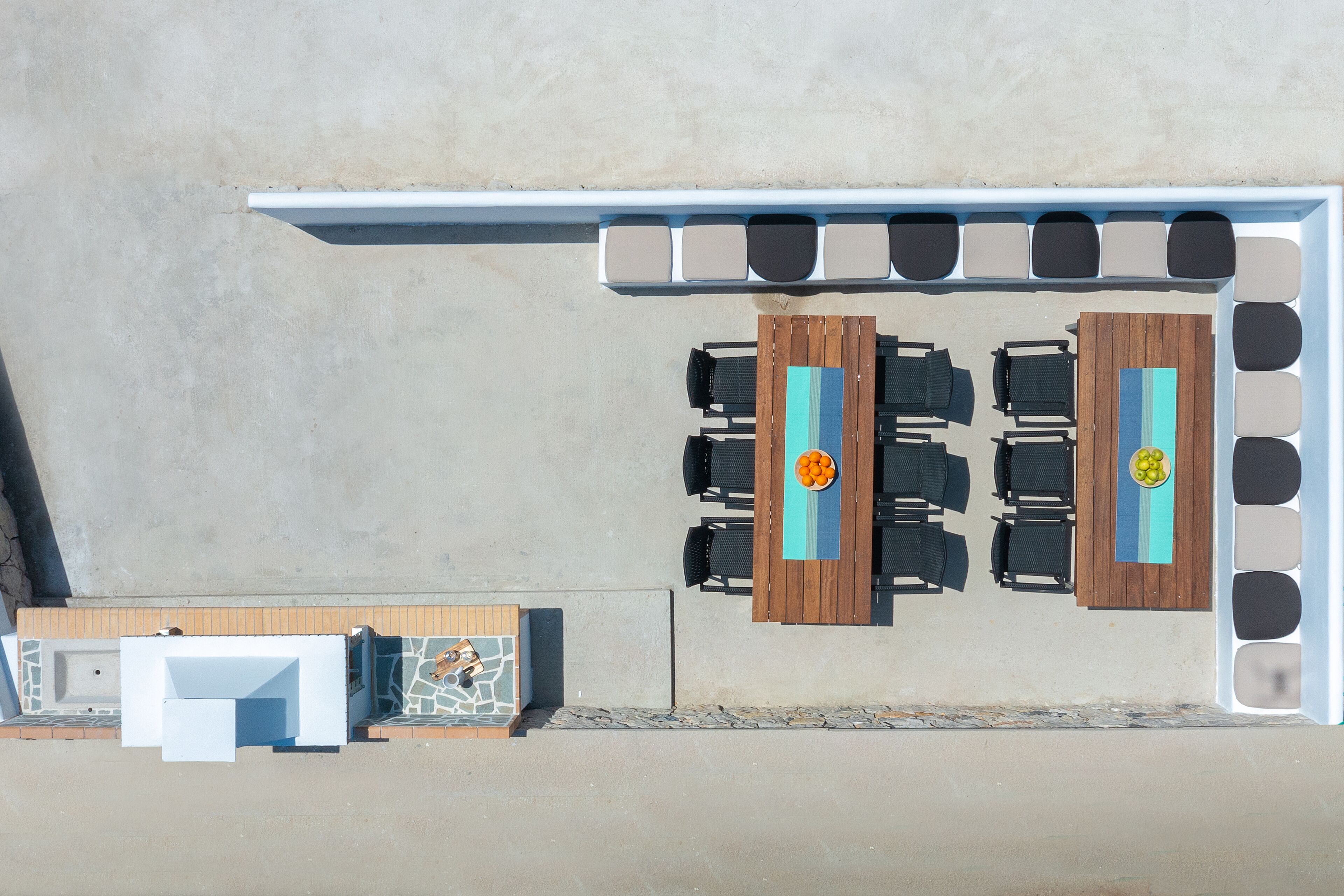 An aerial view of a poolside area with two wooden tables and chairs, a built-in bench, and a seating area with a pool table.