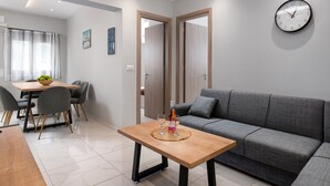 A modern living room with a grey sofa, a wooden coffee table, and a dining area with a table and chairs. - Villa Divina (Rhodes)