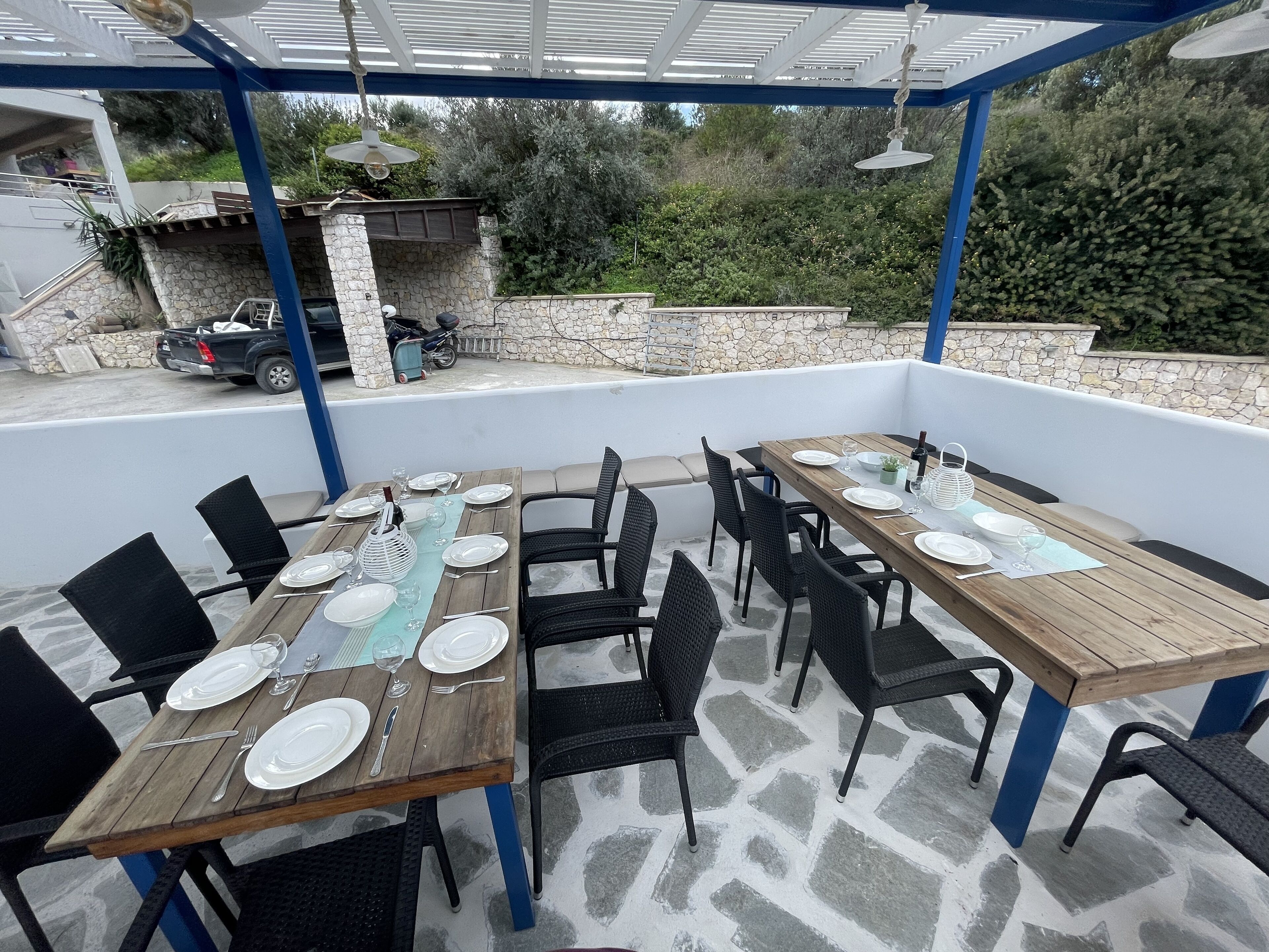Une terrasse extérieure avec deux tables en bois, préparées pour le repas, entourées de chaises noires.