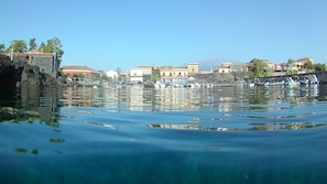 A waterfront view with boats docked, stone buildings, and a clear sky. - The Houses of Carlotta & Giorgia - HOUSE BY THE SEA (Acireale)