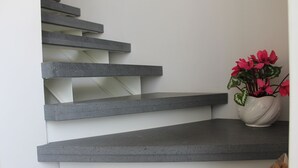 Una escalera moderna con una pared blanca y un jarrón de flores rojas en la plataforma.