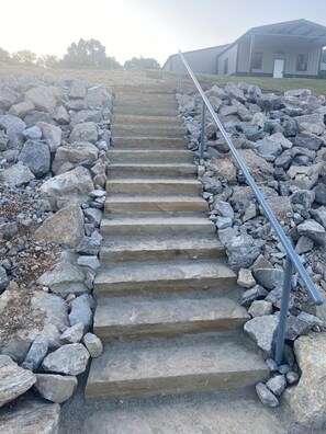 A set of stone steps leading up to a building, surrounded by large rocks and a metal railing.