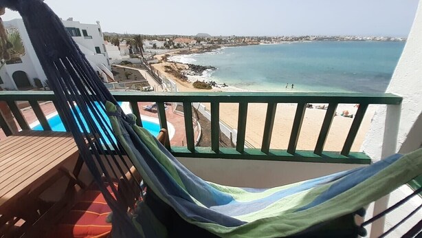 Uma varanda com rede, com vista para uma praia e uma piscina.