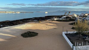 Uma área costeira com praia de areia, litoral rochoso e vista para o mar e montanhas ao longe.