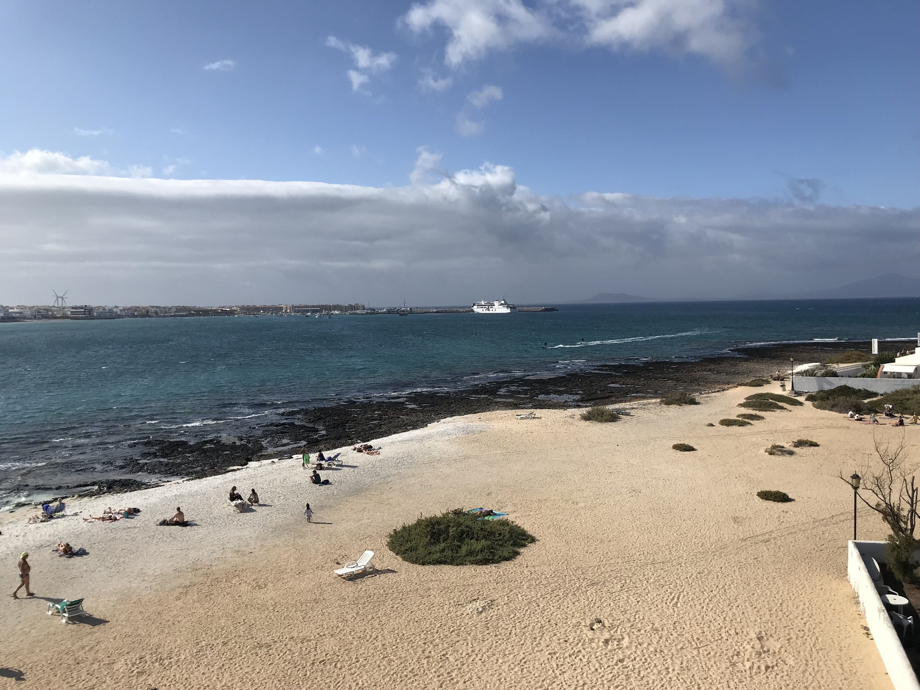 A beach with a sandy shore, a few people, and a ship in the distance.