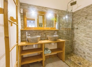 Une salle de bain avec deux vasques en pierre, un meuble-lavabo en bois, une cabine de douche en verre et un miroir avec un cadre en bois.