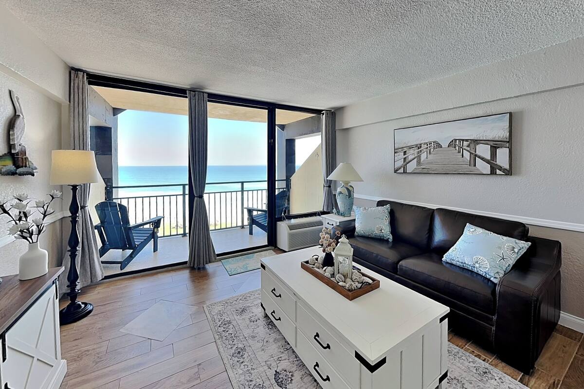A living room with a view of the ocean, a sofa, a coffee table, and a lamp.