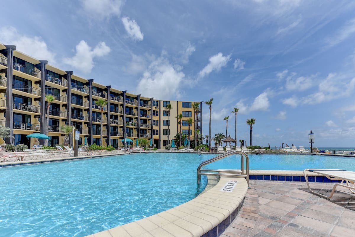 A hotel with a swimming pool, multiple balconies, and palm trees.