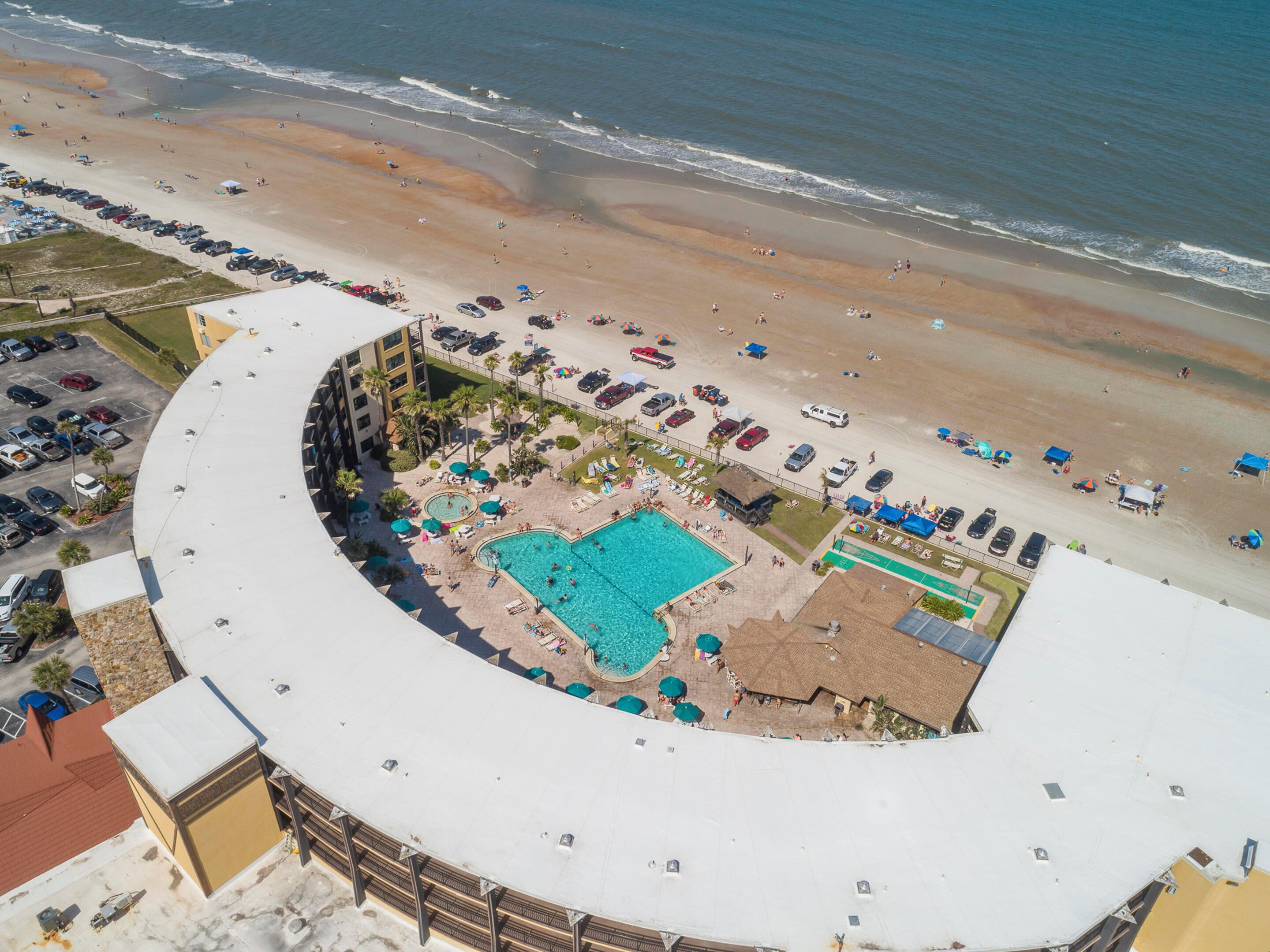Vista aérea de um resort com piscina, praia e área de estacionamento.