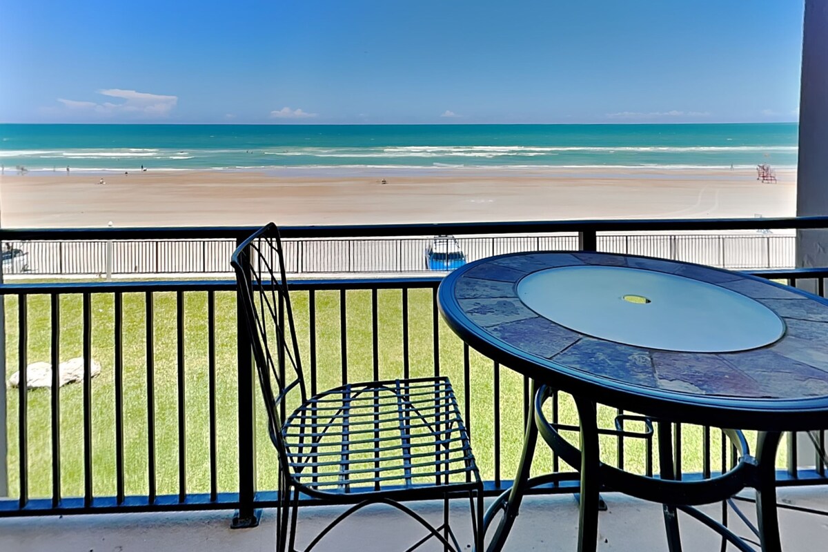 A balcony with a table and chair overlooking a beach.
