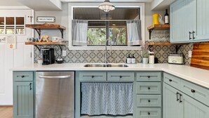 A kitchen with a built-in dishwasher, a coffee maker, and a vintage radio. - Cottage: Fire Pit | Covered Porch | Sleeps 4 | Wimberley TX (Wimberley)