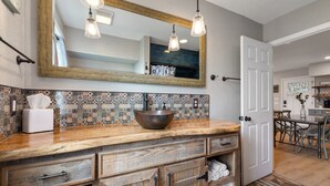 A bathroom with a large mirror, wooden vanity, and a bowl sink. - Cottage: Fire Pit | Covered Porch | Sleeps 4 | Wimberley TX (Wimberley)