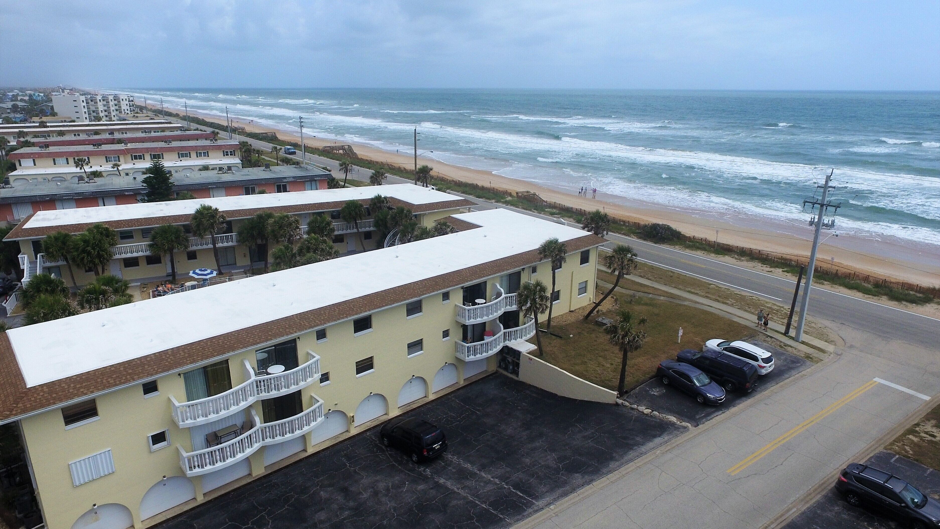 Un hotel de varios pisos con balcones, estacionamiento y vista a la playa y al océano.