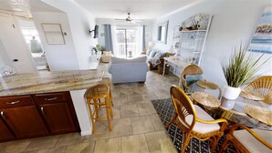 A spacious kitchen with a marble countertop, wooden cabinets, and a dining area with wicker chairs and a glass table. - OCEAN VIEW CONDO w/ Pool, Cable, Wifi, BEACH ACCESS. Ormond-by-the-Sea  (Ormond Beach)